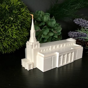 May include: White miniature replica of a temple with a tall spire and a golden finial. The temple has a white dome and a rectangular base.