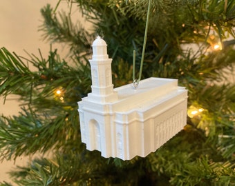 May include: White 3D printed ornament of a church building with a steeple. The ornament is hanging from a green string on a Christmas tree.