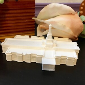 May include: A white 3D printed model of a church building with a tall spire. The model is sitting on a black surface.