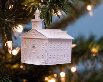 May include: White ceramic ornament shaped like a church building, hanging from a Christmas tree.