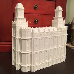 May include: A white 3D printed model of a temple with two tall towers and a large rectangular base.