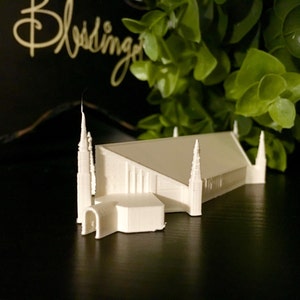 Może przedstawiać: Biały model miniaturowy kościoła z wysokimi wieżami. Model stoi na czarnej powierzchni.