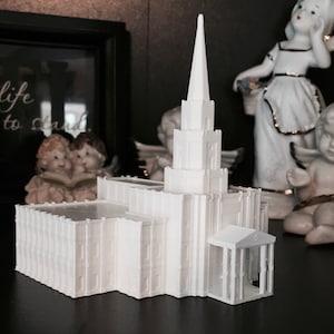 May include: White model of a church with a tall spire and a small porch. The model is made of plastic and is sitting on a dark surface.