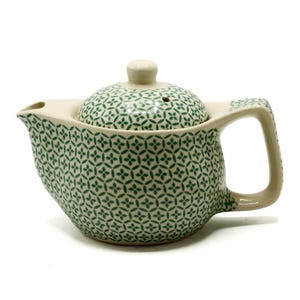 May include: A cream-coloured ceramic teapot with a green floral pattern. The teapot has a matching lid and a curved handle. The spout is on the left side. The teapot is designed for brewing tea.