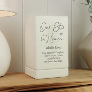 May include: White ceramic memorial candle holder with the text "Our Star in Heaven" and the name "Isabella Rose". The text below reads "Our Beautiful Daughter Forever in our Hearts 12th July 2014 9th December 2025".