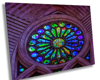 May include: A large, circular stained glass window with a colorful, geometric design. The window is set in a stone archway and is surrounded by a dark purple wall.