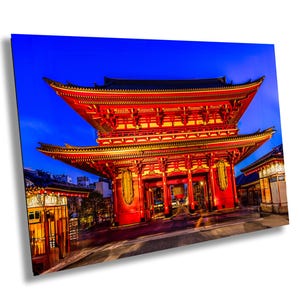 Op de afbeelding: Een traditionele Japanse tempelpoort, of torii, geschilderd in rood en goud. De poort is 's nachts verlicht, met een blauwe lucht op de achtergrond.