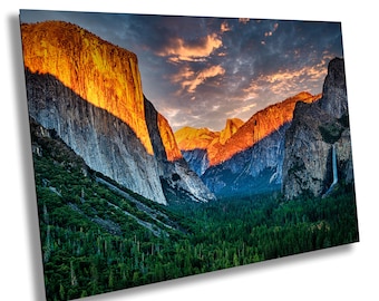 May include: A panoramic view of a mountain range with a valley in the foreground. The mountains are a mix of gray and orange, with a waterfall cascading down one of the cliffs. The valley is covered in a dense forest of evergreen trees. The sky is a vibrant blue with pink and orange clouds.