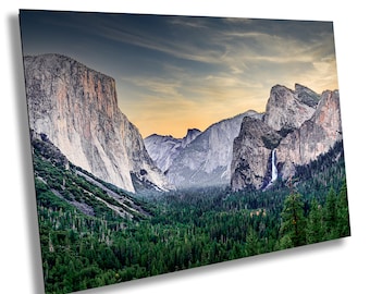 May include: A panoramic view of a valley in Yosemite National Park, California. The image shows a dramatic landscape with towering granite cliffs, lush green forests, and a cascading waterfall. The sky is a mix of blue and orange, creating a beautiful sunset.