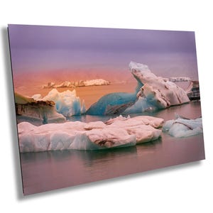 May include: A panoramic view of a frozen lake with large icebergs in shades of blue and white. The sky is a vibrant purple and orange, creating a dramatic and colorful scene.