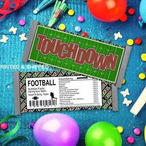 May include: A chocolate bar wrapper with a football field design and the word "TOUCHDOWN" printed in brown letters. The wrapper also includes a nutrition facts label with the heading "FOOTBALL" and a list of football-related skills, such as "Endurance", "Agility", and "Teamwork".
