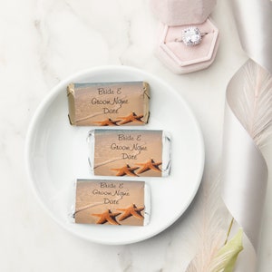 Op de afbeelding: Drie kleine chocolade reepjes verpakt in zilverfolie met een stranddecor en een zeester-ontwerp. De wikkels hebben de tekst "Bride & Groom Name Date" erop gedrukt.