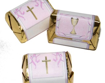 May include: Three small, wrapped chocolate bars with pink and white paper. The paper has a gold cross and a gold chalice design. The wrappers are gold.