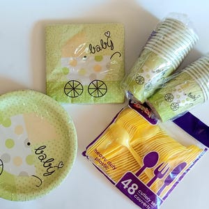 May include: A collection of baby shower party supplies, including a plate, napkins, and cups, all featuring a stroller design in green and white. A package of yellow plastic cutlery is also included.