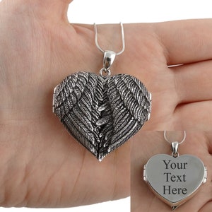 May include: Silver heart-shaped locket necklace with angel wings on the front and a blank space on the back for engraving. The locket is open and the inside is visible. The text "Your Text Here" is engraved on the back of the locket.
