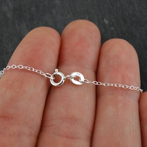 May include: A silver chain necklace with a lobster clasp closure. The chain is made of small, round links. The clasp has a small, round tag with the number "925" on it.