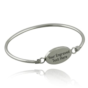 May include: A silver bangle bracelet with an oval-shaped charm that says "Your Engraved Text Here".