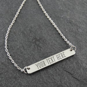 May include: A silver necklace with a long, thin bar pendant that says "YOUR TEXT HERE".