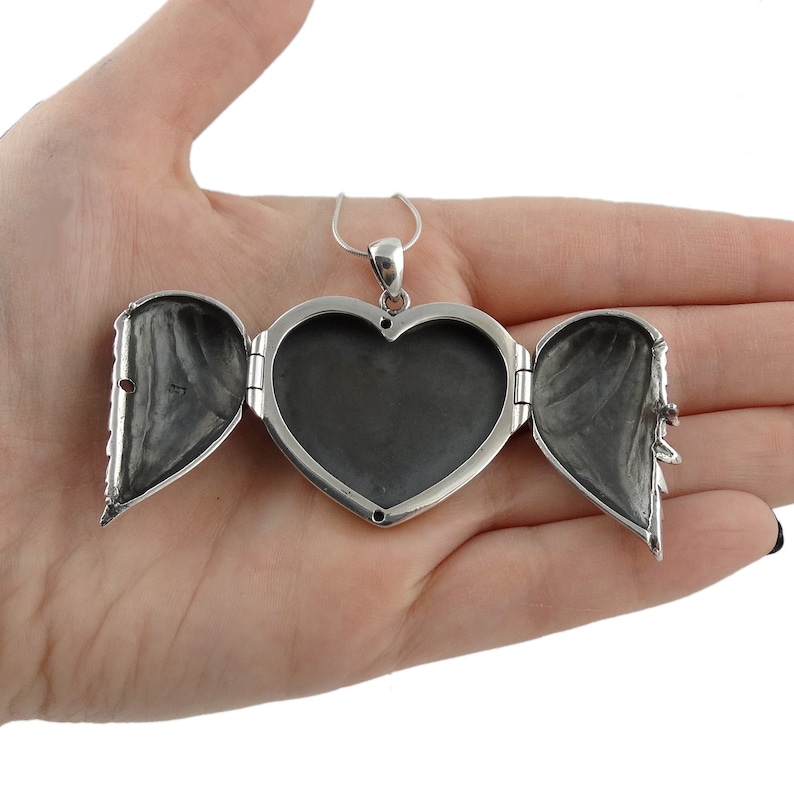 May include: A silver heart-shaped locket necklace with a hinged opening. The locket is open, revealing two empty compartments inside.