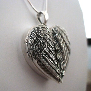 May include: Silver heart-shaped locket with angel wings. The locket is open and the inside is visible.