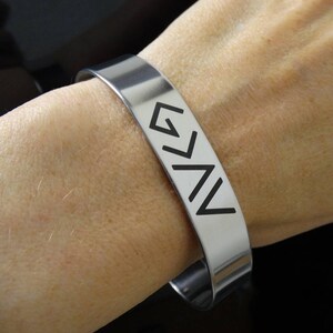 May include: A silver bracelet with the word "God" written in black arrows.