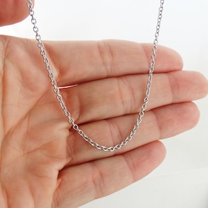 May include: A silver chain necklace with a delicate, thin chain link design. The chain is shown on a hand, making it easy to visualize the length and size.