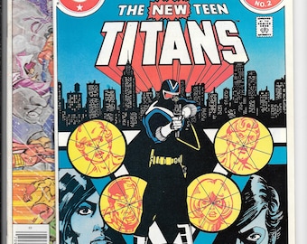 May include: Comic book cover for "Annual The New Teen Titans" featuring a costumed character aiming a weapon. The cover is predominantly blue, red, and yellow, with a cityscape backdrop. The comic is from 1983 and has a price tag of $1.00.