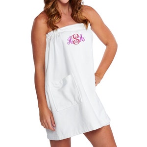 May include: White terry cloth spa wrap with a pocket and a monogram in pink and purple. The wrap is designed to be worn strapless and has a drawstring at the top. The model is wearing the wrap.
