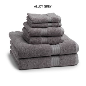 May include: A stack of six gray bath towels with a subtle woven pattern. The towels are folded and arranged in a pyramid shape. The towels are labeled "Alloy Grey".