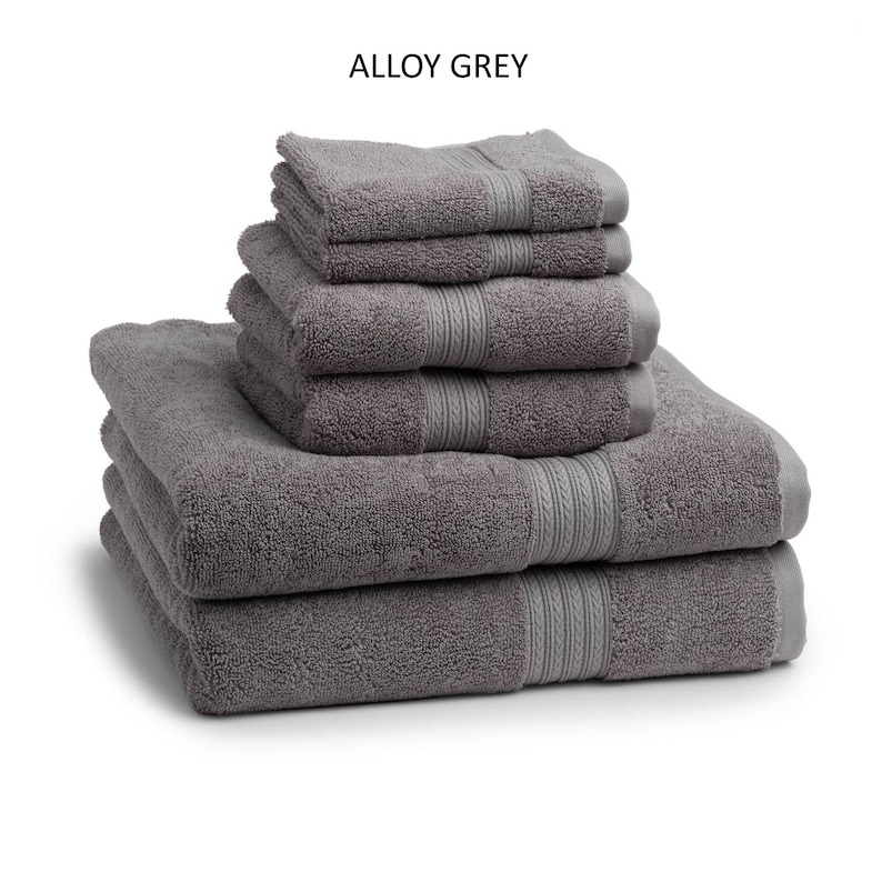 May include: A stack of six gray bath towels with a subtle woven pattern. The towels are folded and arranged in a pyramid shape. The towels are labeled "Alloy Grey".