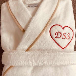 May include: White bathrobe with a beige trim and a red embroidered heart with the initials "DSS" on it.