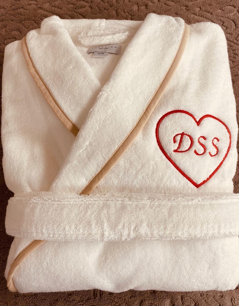 May include: White bathrobe with a beige trim and a red embroidered heart with the initials "DSS" on it.