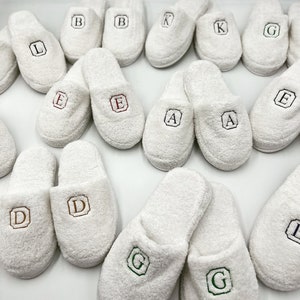 May include: White terry cloth slippers with embroidered letters, including A, B, D, E, G, K, and L.