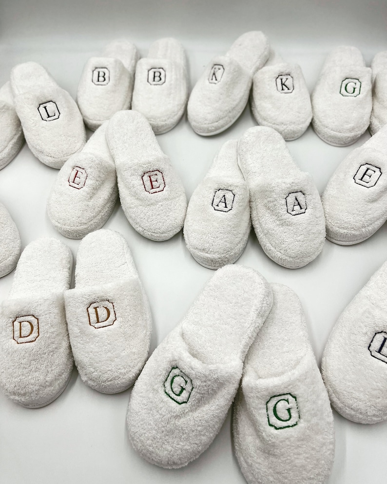 May include: White terry cloth slippers with embroidered letters, including A, B, D, E, G, K, and L.