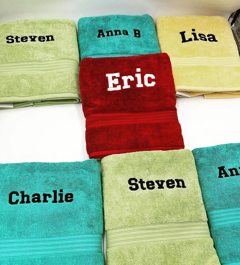 May include: A collection of six towels with embroidered names, including Steven, Anna B, Lisa, Eric, Charlie, and Steven. The towels are in various colors, including green, red, yellow, and blue.