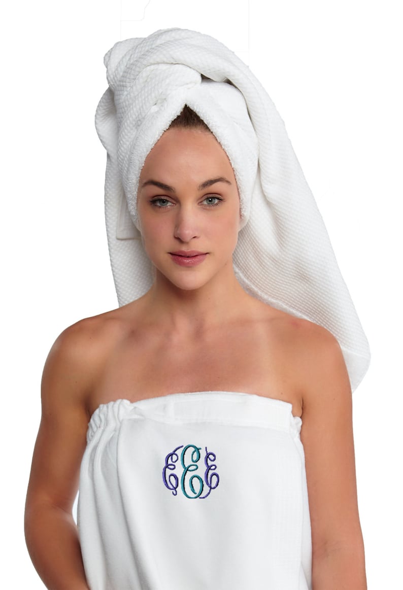 May include: A white spa towel wrap and matching head wrap. The wrap features an embroidered monogram in teal and purple. The woman in the image is wearing the towel wrap and head wrap.