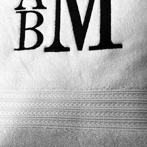May include: White towel with black embroidered letters "A" and "M" with a smaller "B" underneath the "A".