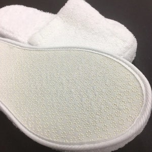 May include: White terry cloth slippers with a white rubber sole featuring a textured pattern of small dots.