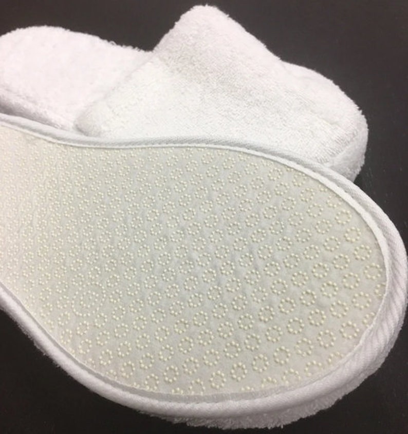 May include: White terry cloth slippers with a white rubber sole featuring a textured pattern of small dots.