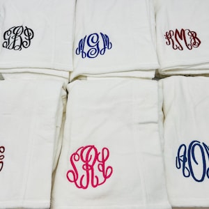 May include: White towels with embroidered monograms in various colors, including black, blue, and red. The towels are folded and stacked, showcasing the personalized initials in a decorative script font. The towels are a soft, plush material.