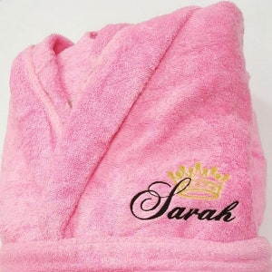 May include: Pink bathrobe with a black embroidered crown and the name "Sarah" on the front.