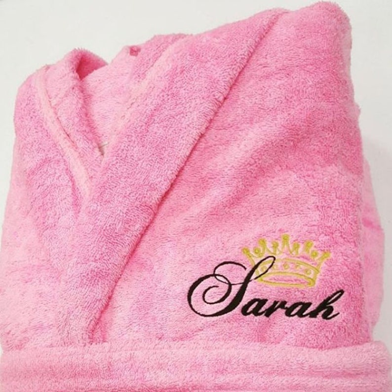 May include: Pink bathrobe with a black embroidered crown and the name "Sarah" on the front.