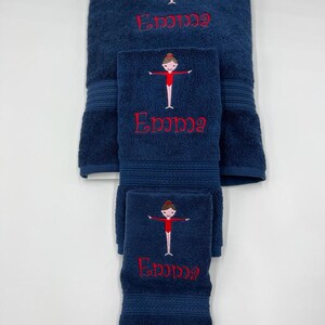 May include: A set of three navy blue towels with embroidered gymnast figures and the name "Emma" in red thread.
