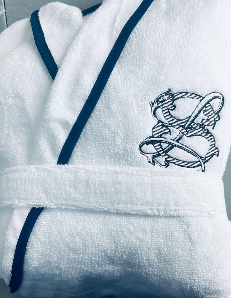 May include: White bathrobe with a navy blue trim and a black embroidered logo on the right side.