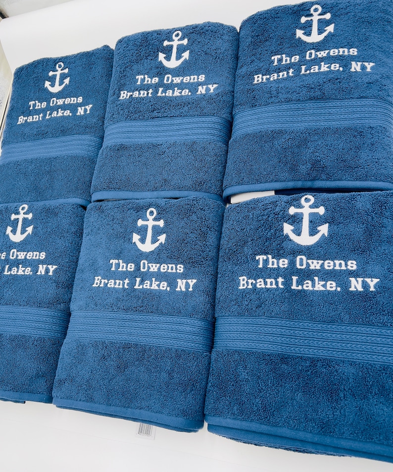 May include: Six blue bath towels with white embroidered anchors and the text "The Owens Brant Lake, NY".