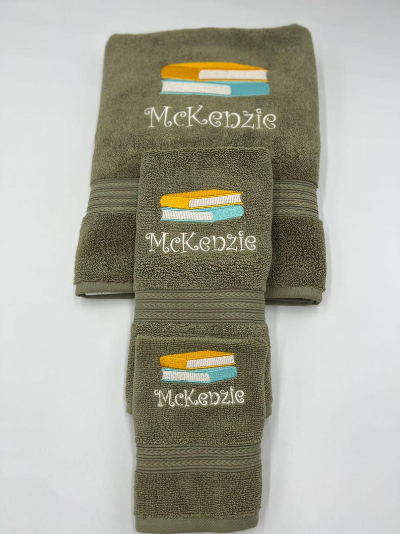 May include: A set of three green towels with embroidered stacks of books and the name "Kenzie".