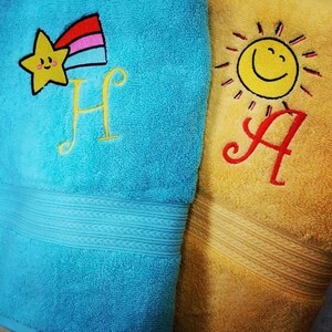 May include: Two embroidered towels, one blue with a yellow star and rainbow, the letter "H" and the other yellow with a yellow sun and the letter "A".