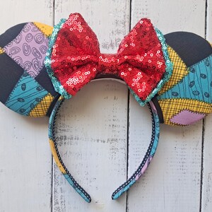May include: Red sequin bow headband with black and blue patchwork fabric ears. The ears are inspired by the character Sally from the movie The Nightmare Before Christmas.