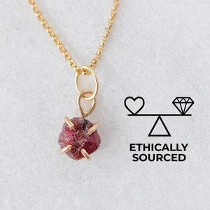 May include: A delicate gold chain necklace featuring a raw ruby pendant. The ruby is a deep red colour and has a natural, unpolished look. The necklace is ethically sourced.