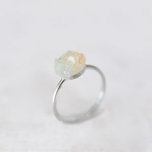 May include: A silver ring featuring a white opal gemstone set in the centre. The opal has an irregular shape and a milky white colour with iridescent flashes of colour.